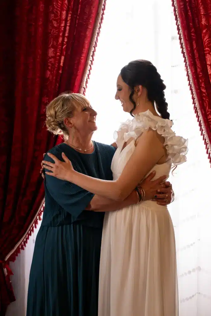 Bride And Mother Hugging On Day Of Wedding Inside Reception Hall
