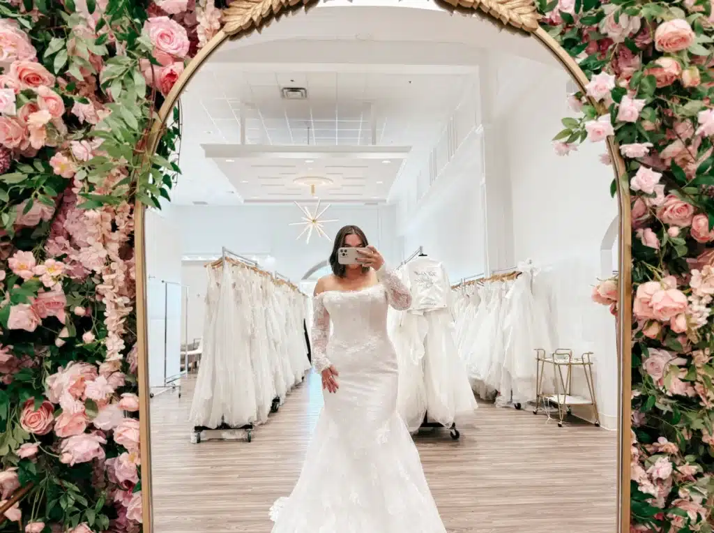 Bride Trying On Fit And Flare Wedding Dress With Lace Long Sleeves Posing In Front Of Mirror In Indianapolis