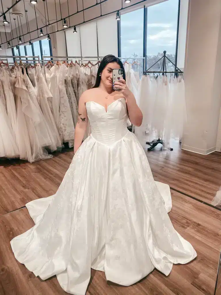 Bride To Be Taking A Mirror Selfie While Trying On An Ivory Basque Waist Wedding Dress