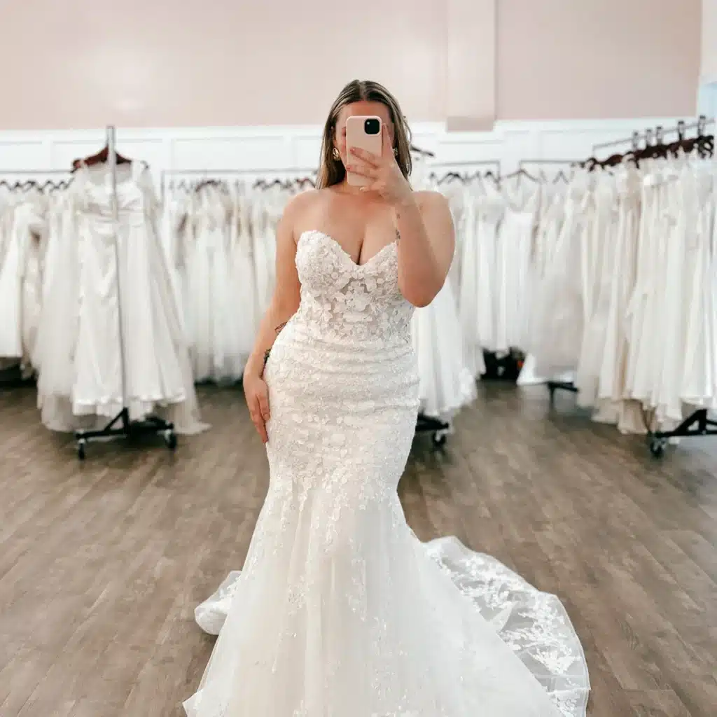 Bridal Client Posing In Mirror Trying On Fit And Flare Lace Wedding Dress