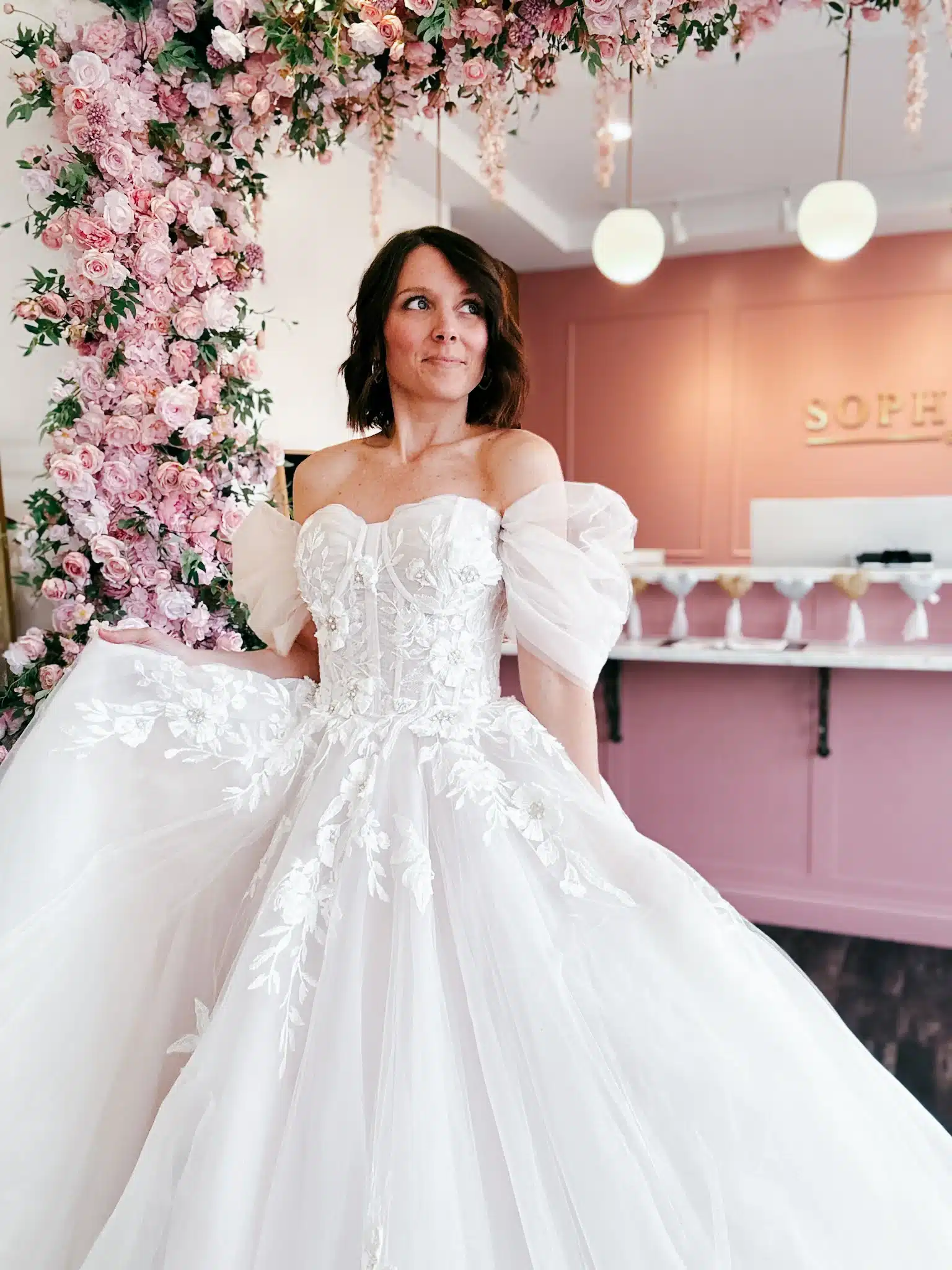 Bride Trying On Floral White Wedding Dress With Ruched Off The Shoulder Sleeves Bride Trying On Floral White Wedding Dress With Ruched Off The Shoulder Sleeves