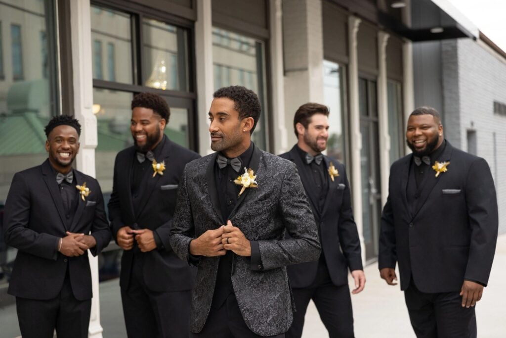 Groom and groomsmen wearing coordinated black wedding suits and tuxedos