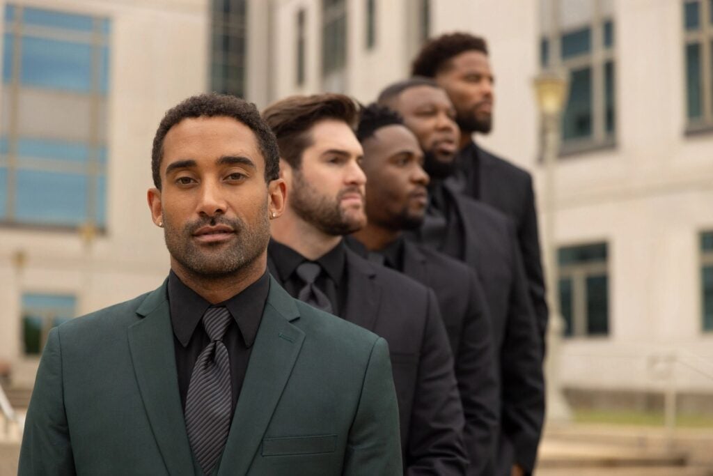 Groom in a dark green suit with black tie alongside groomsmen in black suits