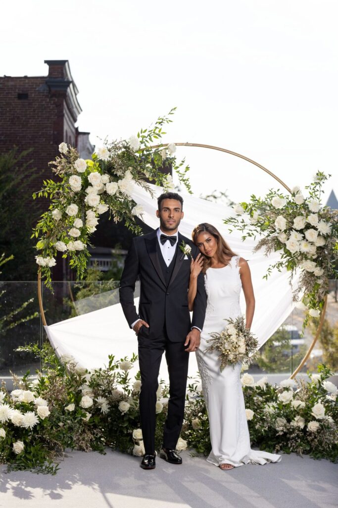 Groom wearing a black tuxedo beside his bride at an outdoor wedding ceremony