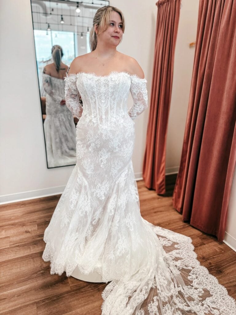 Bride wearing an off-the-shoulder lace wedding gown with sheer sleeves, a fitted bodice and a dramatic train